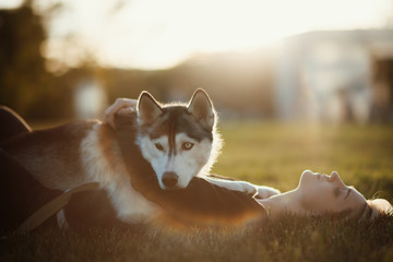 Beautiful young woman playing with funny husky dog outdoors in park at sunset  or sunrise 
