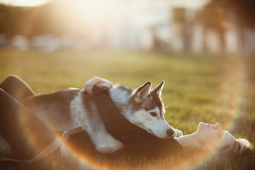 Beautiful young woman playing with funny husky dog outdoors in park at sunset  or sunrise 