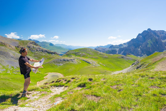 Hiker reading trekking map while resting at panoramic mountain spot. Outdoors activities, summer adventures and exploration on the Italian French Alps. Expansive view from the top.