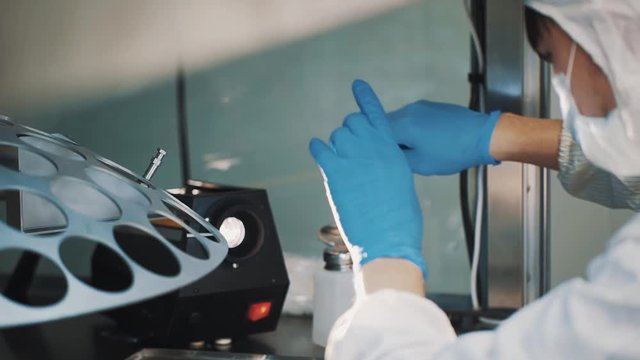 Optician in white robe blue rubber gloves cleaning lens with cotton swab at manufacture metal desk