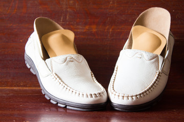White leather slipper or shoes with orthopedic insoles. Wooden background.