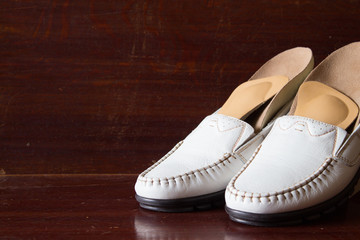 White leather slipper or shoes with orthopedic insoles. Wooden background.