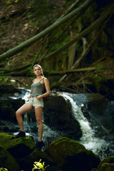 Hiking in forest with waterfall in background. Woman trekking in mountains against waterfall. Female with backpack on hike in nature. Cascading waterfall