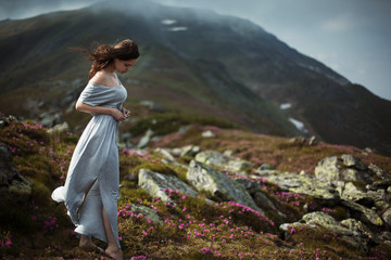Naklejka na ściany i meble Perfect brunette woman on a mountain. Beauty woman with perfect vintage dress background mountains. Blooming rhododendron in cloudy weather