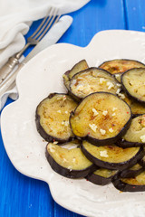 fried eggplant with garlic on white plate on wooden background
