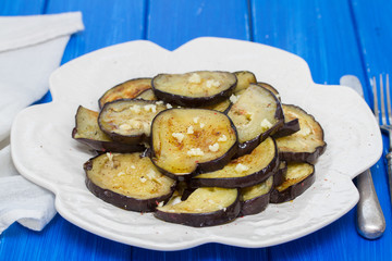 fried eggplant with garlic on white plate on wooden background
