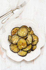 fried eggplant with garlic on white plate on wooden background