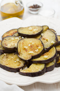 fried eggplant with garlic on white plate on wooden background