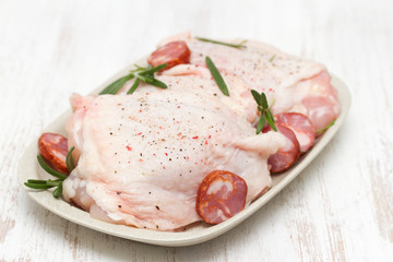 raw chicken with smoked sausage and rosemary on white dish