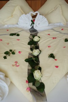 Flitterwochen: romantische Bettdekoration im Hotelzimmer (Schwäne und Rosenblüten)