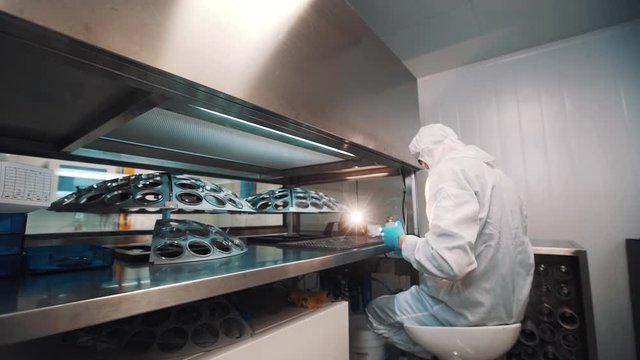 Caucasian man engineer in sterile white clothes in laboratory manages glass lenses on special metal device