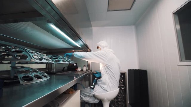 Caucasian man optician in sterile white clothes in laboratory manages glass lenses on special metal device