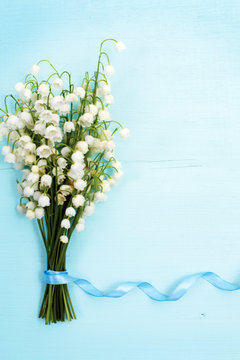 Beautiful floral frame with lilies of the valley flowers on blue wooden table.