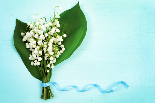 Beautiful floral frame with lilies of the valley flowers on blue wooden table.