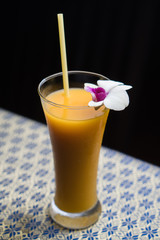 Mango smoothie with straw and orchid flower isolated on the table with traditional Thai tablecloth over black background