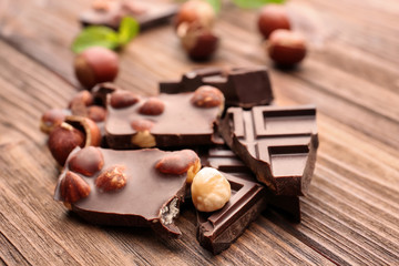 Broken chocolate pieces with nuts and mint leaves on wooden table