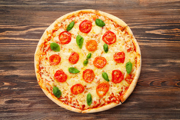Delicious pizza with tomatoes, basil and melted cheese on wooden background