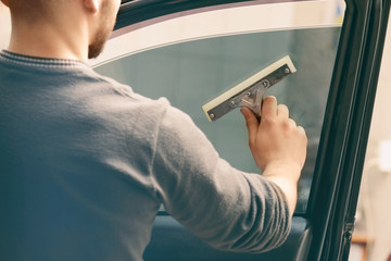 Worker applying tinting foil onto car window