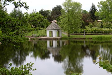 The white gazebo in the park reflecting of the water of the lake.