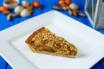 Homemade apple pie sliced on square plate with kumquats and almonds on blue wooden background