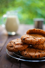 Stack of chocolate chip cookie and glass jug of milk on rustic wooden table,vertical image