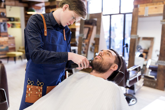 man and barber with trimmer cutting beard at salon