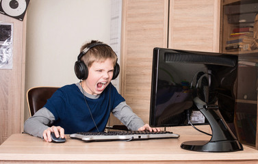 Gaming, entertainment, technology, let's play concept. Angry screaming pre teen boy  in headset with pc computer playing game at home