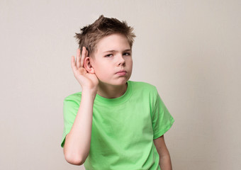 Human face expression, emotion, body language. Curious preteen boy listens. Closeup portrait child hearing something, parents talk, gossips, hand to ear gesture.