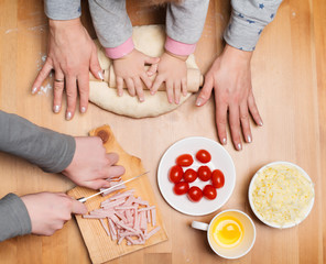 Cooking with children. Making pie at home. Children and mother hands knead and roll dough with a rolling pin on the table.
