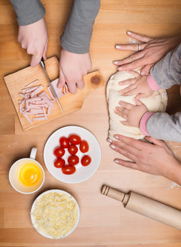 Cooking with children. Child and mother hands knead and roll dough with a rolling pin on the table.