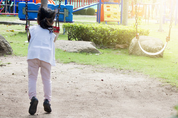 The girl swings alone by turning her back on her.