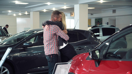 Man Standing Behind Woman and Covering Her Eyes While Standing in front of Shiny New Red Vehicle Inside Car Dealership - Man Surprising Woman with New Car in Show Room.