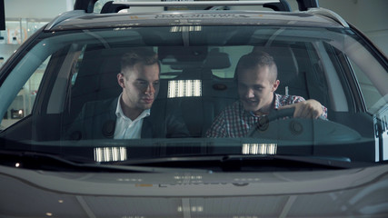 Front window of brand new automobile with lights reflecting on glass in showroom. The buyer and...