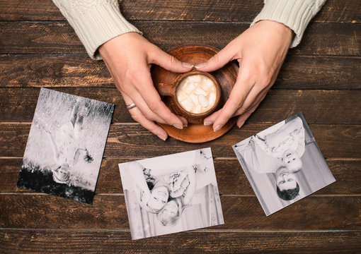 Memories concept. Family photos and cup of coffee or cocoa in female hands on wooden background. Top view.