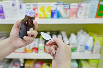 Hand holding a cough syrup bottle in pharmacy drugstore.