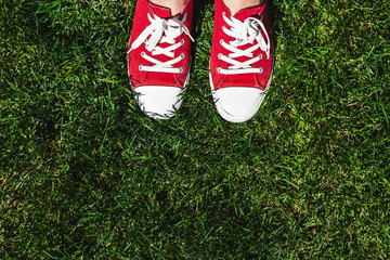 Legs in old red sneakers on green grass. View from above. The concept of youth, spring and freedom