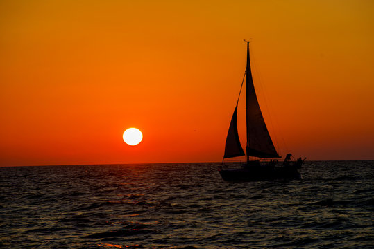 full sail sailing boat against ocean sunset