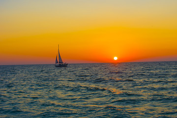 full sail sailing boat against ocean sunset