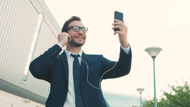 Attractive businessman video cahtting on smartphone outside near office center building. Man having video call with collegues, family. Close up
