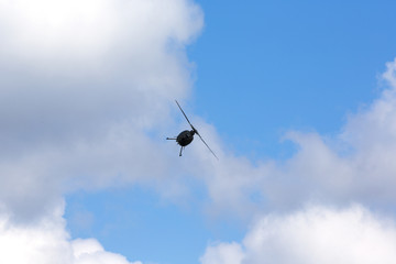 Helicopter hovering against a blue sky with clouds. The copter looks like a silhouette.