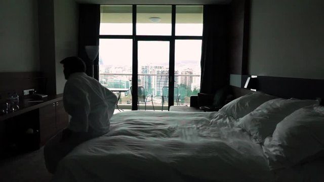 Slow motion. Happy man jumping on bed at hotel in bathrobe. Cool apartments relaxation. Concept relax after hard working. Holiday. 960 fps