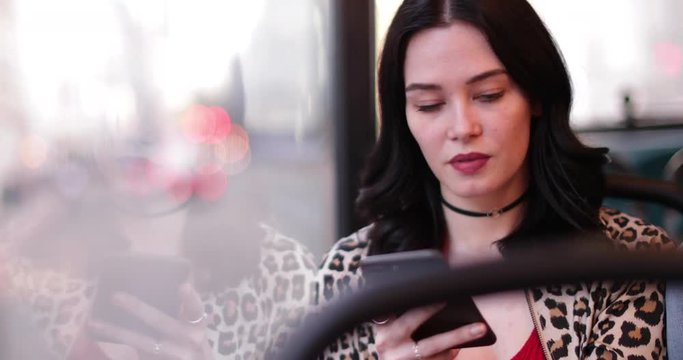 Young adult female travelling on bus looking at smartphone