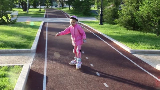 A girl of seven years old learns to skate in the park on a bicycle path