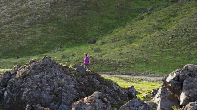 Wide tracking shot of woman running on mountain path. Iceland