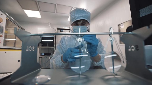 Engineer caucasian man in sterile clothes, face mask and rubber gloves puts magnifier lenses on special metal holder at laboratory