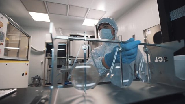 Optician caucasian man in sterile clothes, face mask and rubber gloves puts magnifier lenses on special metal holder at laboratory