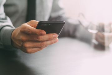 close up of businessman working with mobile phone and eyeglass on wooden desk in modern office