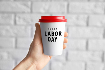 Female hand holding paper cup on blurred brick wall background
