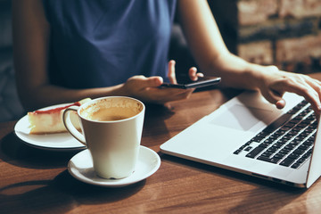 Business woman holding a phone and working on a laptop in a cafe