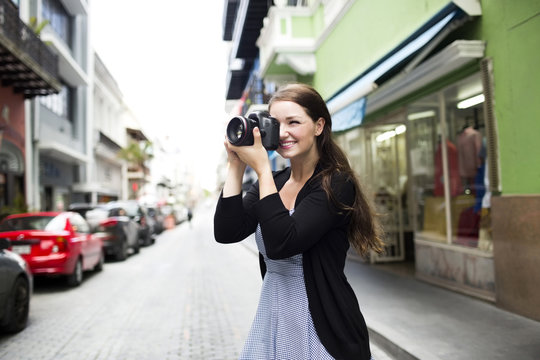 Smiling woman taking picture with camera while standing at outdoors